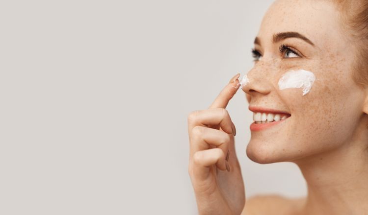 Femme se mettant de la crème sur le nez et
les pommettes et arborant un grand sourire